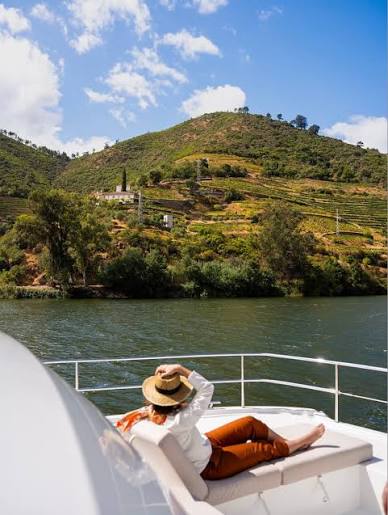 Um viajante a descansar no convés de um barco no Vale do Douro, entre as vinhas
