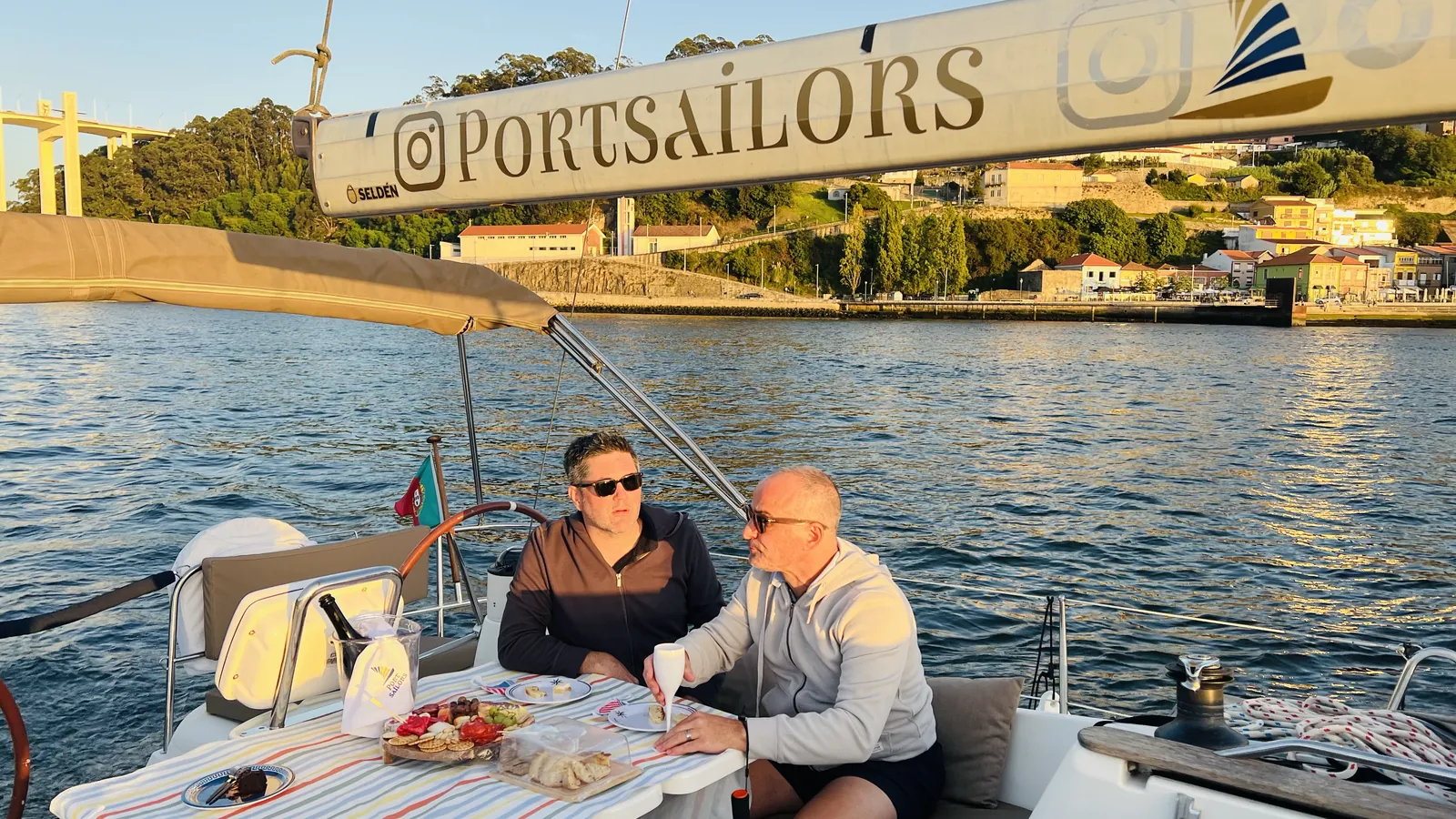 Casal a almoçar no convés enquanto o veleiro passa sob a Ponte da Arrábida no Porto