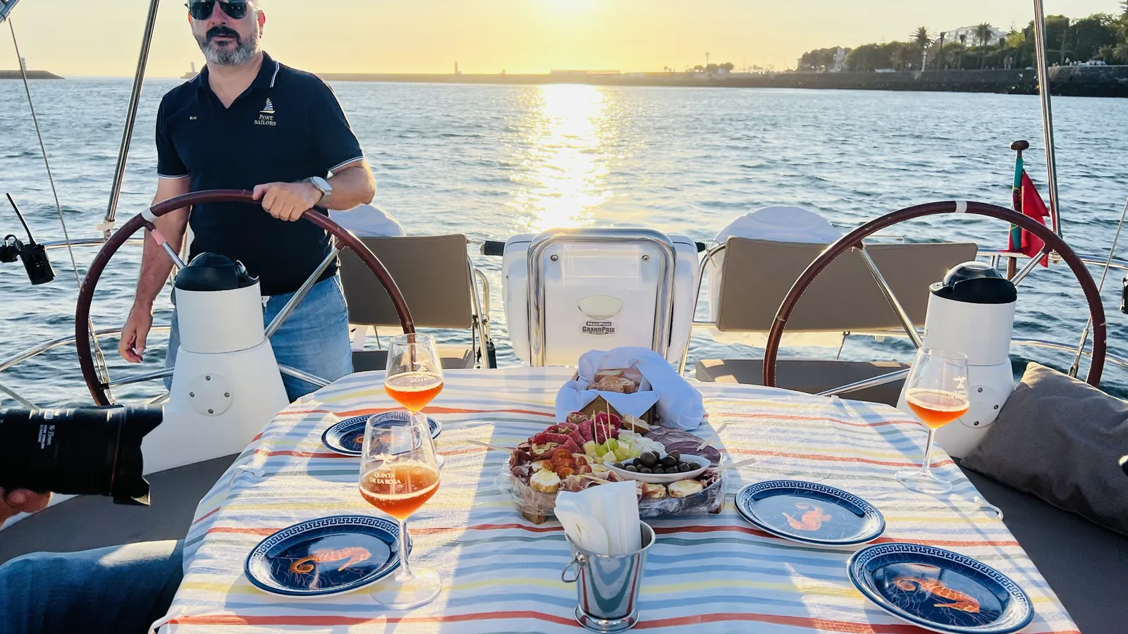 Capitão ao leme junto a uma mesa posta num cruzeiro privado ao pôr do sol no Porto, sobre o Douro