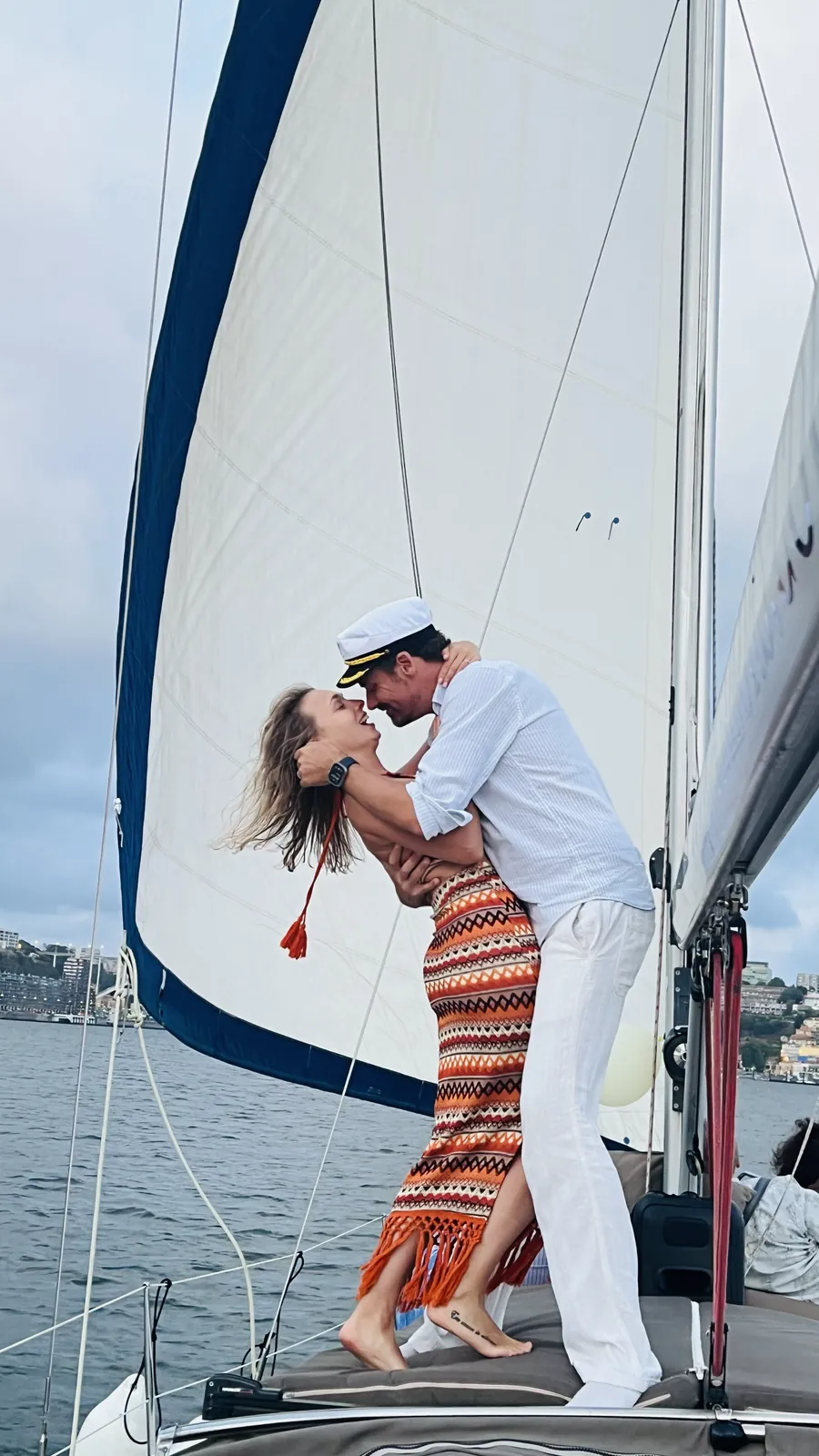 Casal abraçado sob a vela branca num cruzeiro à vela romântico no Porto