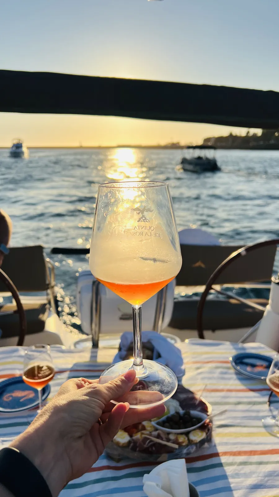 Copo de vinho rosé erguido sob a Ponte da Arrábida ao pôr do sol no Porto