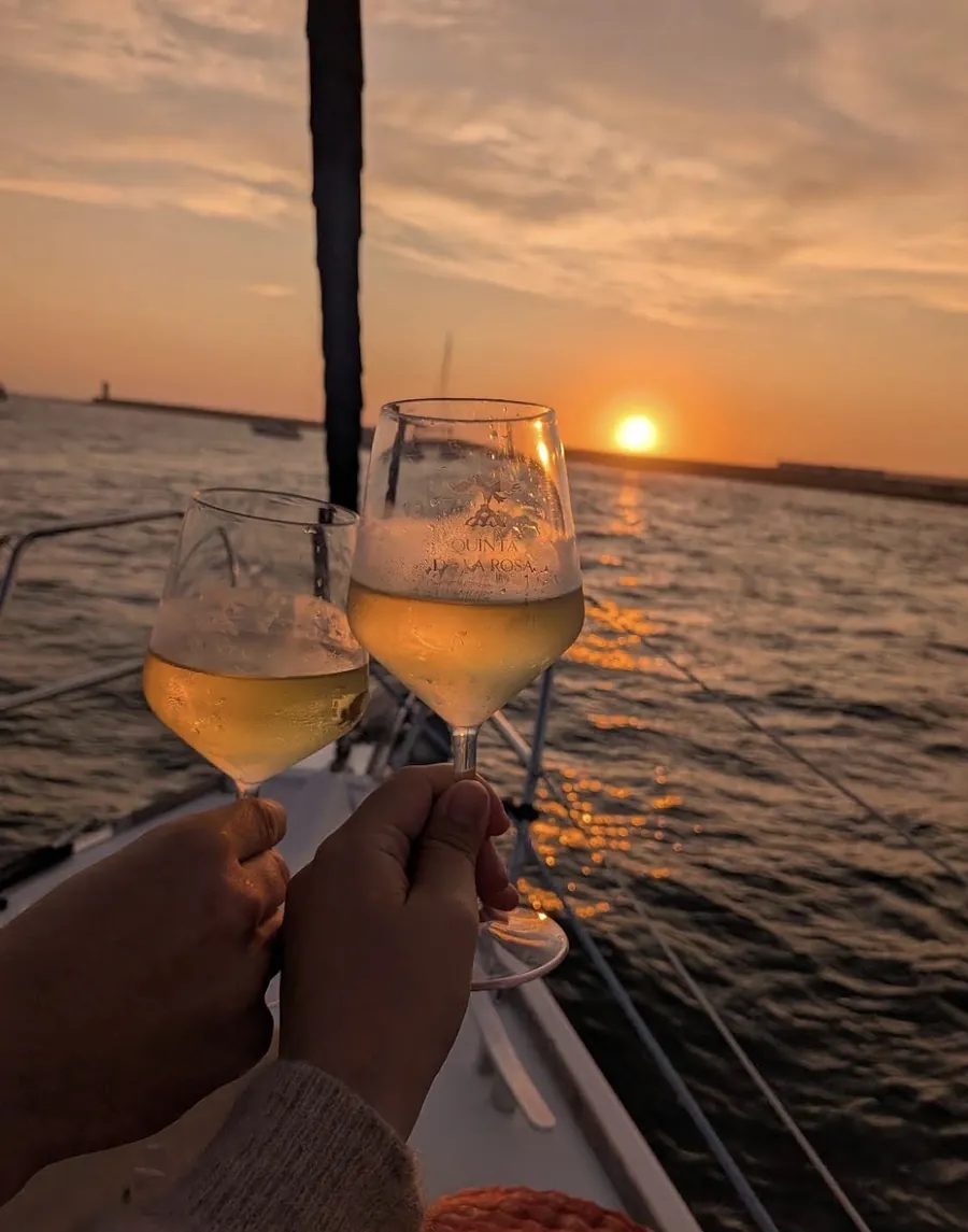 Dois clientes a brindar com vinho rosé enquanto o sol se põe sobre o Atlântico num cruzeiro à vela no Porto