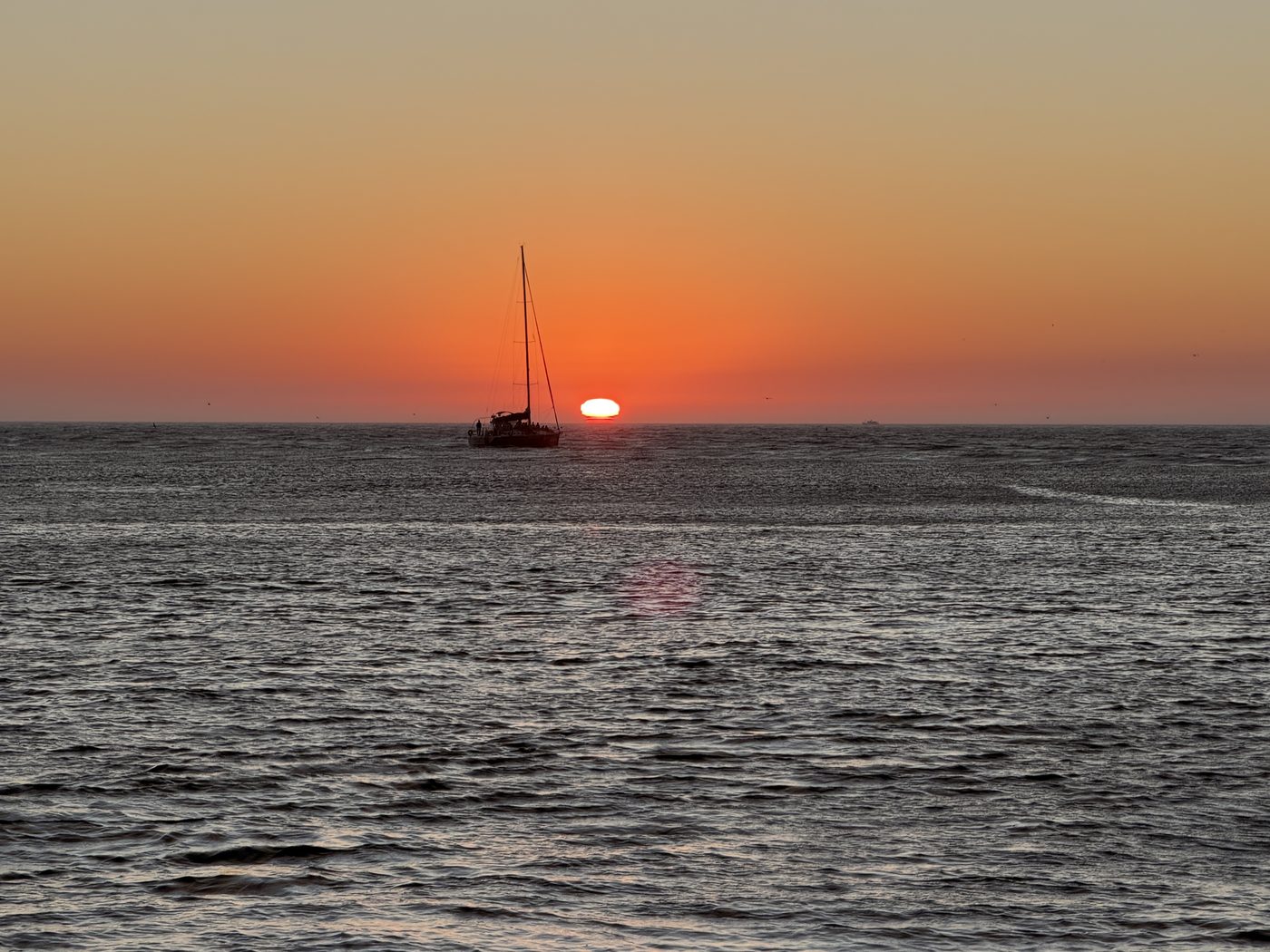 A sailboat silhouetted against the setting sun on the Atlantic horizon off Porto in autumn
